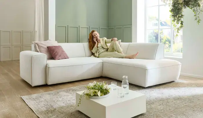 Frau sitzt beim telefonieren auf einem weißem Ecksofa mit Kissen